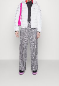 Vit pufferjacka, svart långärmad tröja, grå byxor med breda ben och zebramönster, svarta och rosa plattformsskor samt en rosa axelväska.