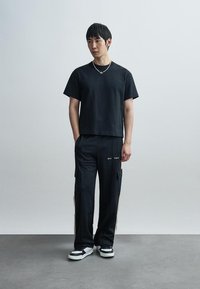 Μαύρο βαμβακερό T-shirt με άνετη εφαρμογή, συνδυασμένο με μαύρο cargo παντελόνι με πλαϊνές τσέπες και μπεζ λεπτομέρειες. Λευκά παπούτσια ολοκληρώνουν την εμφάνιση.