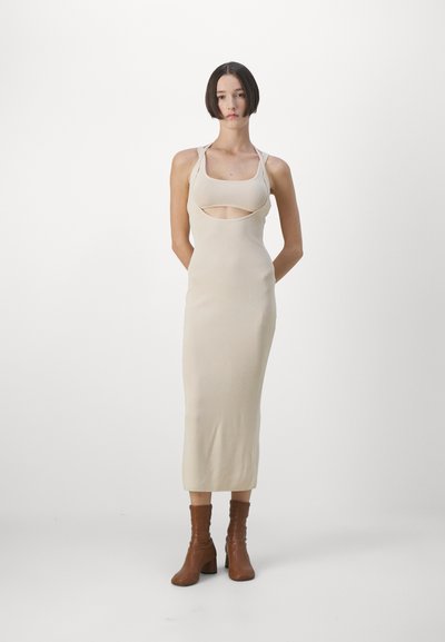Beige sleeveless dress with cutout detail, midi length, made of ribbed fabric. Paired with brown ankle boots. Simple, fitted design.