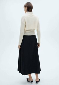 Pulover din tricot ribbed, de culoare fildeș, cu guler înalt, design stratificat peste o fustă neagră, cu lungime până la glezne, fluidă. Pantofi cu toc negru completează ținuta.