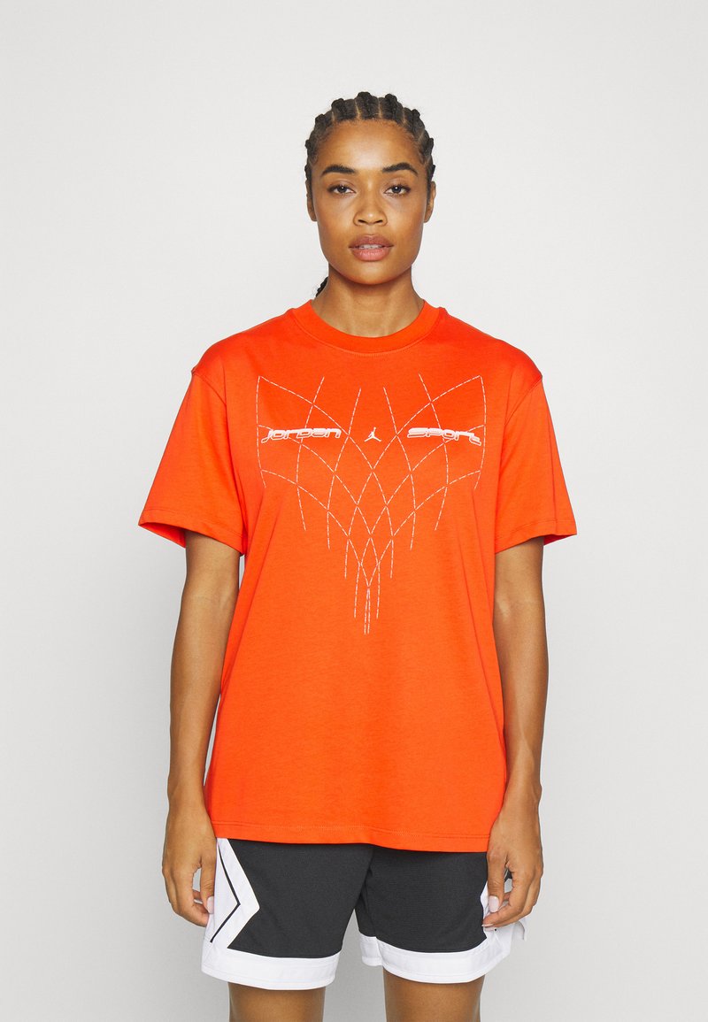 T-shirt orange à manches courtes avec un design graphique géométrique blanc sur le devant, en coton et avec une coupe décontractée. Associé à un short noir.