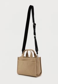 Krémszínű vászontáska rövid fogantyúkkal és fekete, állítható vállpánttal. Elöl zseb található, és a tartósság érdekében textúrált anyagból készült.