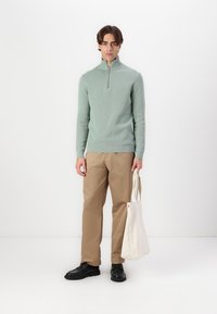 Mint green quarter-zip sweater made of knitted fabric, paired with beige straight-legged pants and black footwear, carrying a cream tote bag.