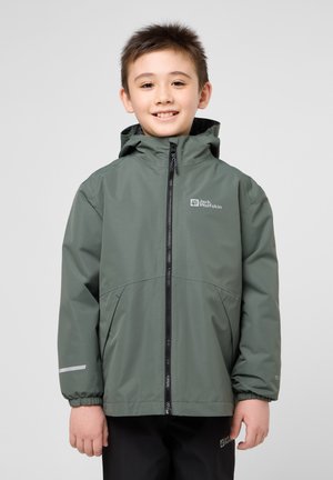 Giacca impermeabile verde con cappuccio, zip frontale e polsi elastici. Presenta un logo sul petto e dettagli riflettenti sulle maniche.