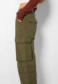 Olijfgroene cargo broek met meerdere grote zakken, recht gesneden ontwerp en duurzaam materiaal. Kenmerken zijn zichtbaar stiksels en een relaxte pasvorm.