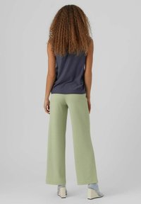Top senza maniche blu navy abbinato a pantaloni larghi verde chiaro, con una texture liscia e una vestibilità rilassata, visto da dietro.