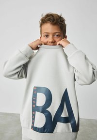 Hellgrauer Sweatshirt mit hohem Kragen und oversized Passform, versehen mit einem großen blauen und orangenen Grafikdesign auf der Vorderseite.