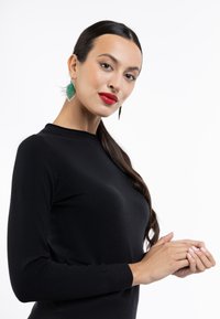 Sort langærmet bluse med en rund halsudskæring, der har en glat overflade. Modellen bærer grønne øreringe formet som blade og har lyse neglelak.