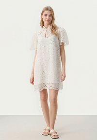 Fehér broderie anglaise ruhá,f magas gallérral, rövid puffos ujjakkal és ívelt szegéllyel. Hímzett pamut anyagból készült, könnyű és légies.