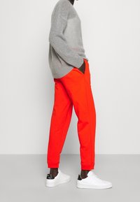 Grå stickad tröja med lös passform, tillsammans med ljus orange svettbyxor med elastiska manschetter. Vita sneakers med svarta accenter.