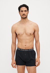 Caleçons en coton noir avec une taille élastique, présentant un texte blanc. La coupe est ajustée et le tissu semble doux et lisse.
