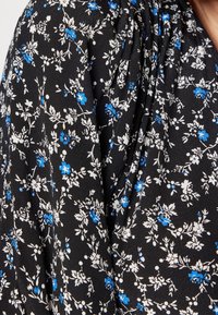 Tissu noir avec de petits motifs floraux en bleu et blanc, présentant une texture plissée qui met en valeur le design délicat et le matériau doux.