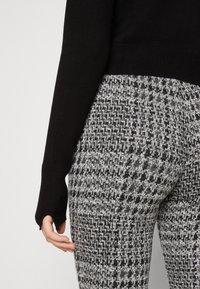 Czarny sweter z długimi rękawami w zestawie z szaro-czarnymi spodniami w wzory z teksturowanym deseniem w jodełkę.