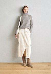 Suéter de cuello alto de canalé gris con mangas largas, combinado con una falda midi de color crema con una abertura frontal. Botines de cuero marrón con cordones.