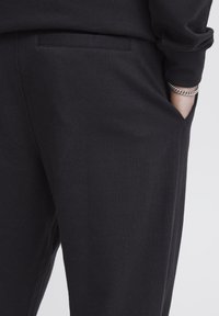 Schwarze Baumwollhosen mit Seitentasche und glatter Textur, in lässigem Schnitt und minimalistischem Design.