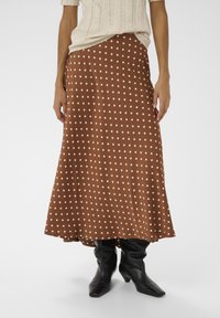 Brun nederdel med hvide polkaprikker lavet af glat stof, der har et flydende design med en lang kant, kombineret med sorte, løstsiddende knælange støvler.