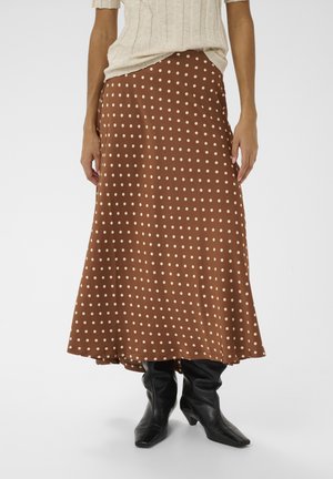 Brauner Rock mit Tupfenmuster aus glattem Stoff, mit fließendem Design und langem Saum, kombiniert mit schwarzen, lässigen kniehohen Stiefeln.