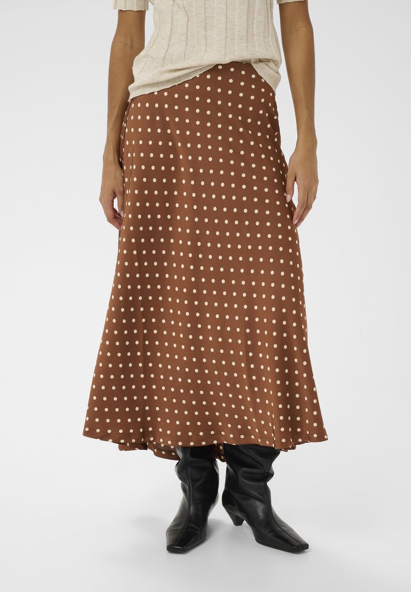 Brun nederdel med hvide polkaprikker lavet af glat stof, der har et flydende design med en lang kant, kombineret med sorte, løstsiddende knælange støvler.