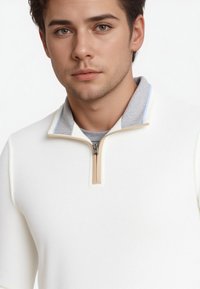 Weißer Zip-Pullover mit strukturierter Oberfläche, grauem Kragen und hellblauen Akzenten. Mit einem sandfarbenen Reißverschluss und einem mehrlagigen Look.
