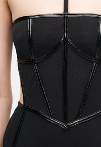 Μαύρο εφαρμοστό bustier με λαμπερά μαύρα διακοσμητικά και λεπτό ιμάντα ώμου σε λευκό δέρμα, εμφανιζόμενο από το στήθος έως τη μέση.