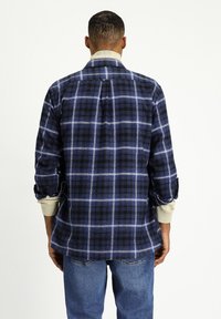 Camicia a maniche lunghe a quadri in blu scuro e nero; presenta linee bianche, colletto e polsini arrotolati. Tessuto morbido.