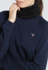 Felpa navy con superficie tessurizzata, dotata di scollo rotondo e polsini a costine. Scaldacollo nero con logo "icebreaker" in rilievo.