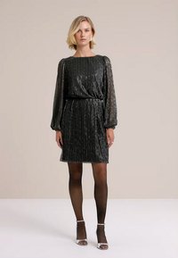 Rochie neagră cu un finisaj metalic texturat, mâneci lungi din material transparent, talie elastică, lungime până la genunchi, asociată cu colanți negri și tocuri argintii.