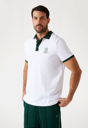 White polo shirt with a green collar and cuffs, featuring an embroidered logo on the left chest. Smooth cotton material, standard fit.