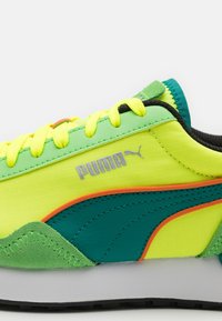 Ungdomssneakers med en livlig gul mesh-överkropp, gröna mocka- och läderdetaljer, en svart sula och framträdande Puma-logotyp.