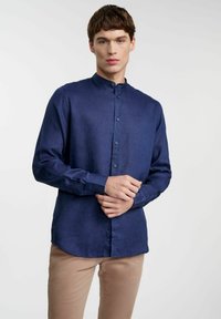Granatowa koszula zapinana na guziki, wykonana z lekkiego materiału, z stójką, z subtelnym logo i długimi rękawami podwiniętymi na mankietach.