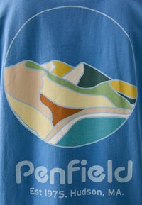 Mėlynas marškinėliai su apvalia grafika, vaizduojančia abstractinius kalnus žalia, geltona ir ruda spalvomis, su tekstu "Penfield" apačioje.