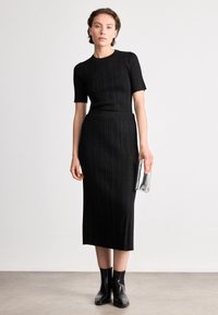 Rochie tricotată neagră, cu mâneci scurte, bust ajustat și fustă midi; asortată cu o poșetă metalică argintie și cizme negre până la gleznă.