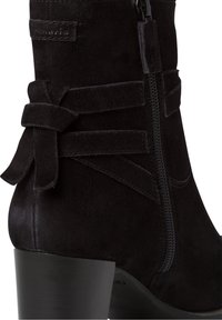 Stivale alla caviglia in suede nero con tacco a blocco, dotato di una cerniera laterale e tie decorative in tessuto vicino alla parte superiore. Texture liscia e design elegante.