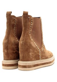 Brązowe zamszowe botki za kostkę z elastycznymi panelami bocznymi, zdobione dekoracyjnymi srebrnymi nitami i solidną podeszwą z krepy. Teksturowane wykończenie i zaokrąglony czubek.
