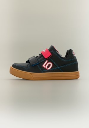 Zapatilla negra y marrón con tiras de velcro rojas y negras, costuras azules y logo blanco de "IQ" en el lateral.
