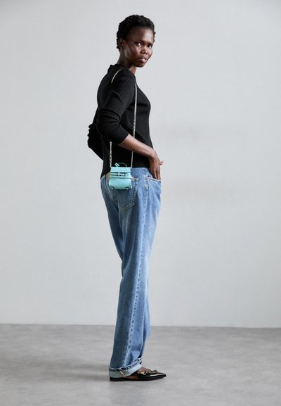 Ribbed black long-sleeve top paired with light blue high-waisted jeans. A small turquoise bag with a chain strap hangs from the waist.