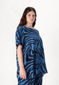 Mėlyna viršutinė su tamsiai mėlynomis zebra juostelėmis, su plačiu apykakle ir trumpomis rankovėmis. Pagaminta iš minkštos medžiagos, turi laisvą, patogią išvaizdą.