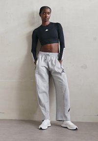 Top cropped a maniche lunghe nero con dettagli bianchi abbinato a pantaloni felpati grigi con cintura elastica e un piccolo logo. Sneakers bianche.