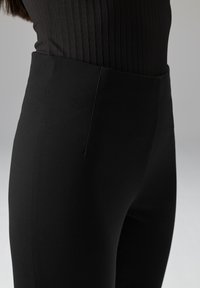 Zwarte broek met hoge taille gemaakt van glad, rekbaar stof. Kenmerkt zich door een aansluitend ontwerp en een gestroomlijnde silhouet.