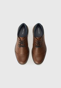 Chaussures en cuir marron avec une finition lisse, design traditionnel à lacets, bout arrondi, et accents de doublure et de semelle en marine contrastants.