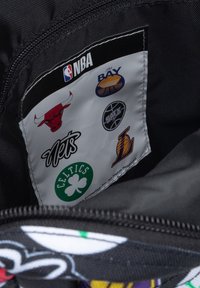 Interior de bolsa de tela negra con logotipos de equipos de la NBA sobre un fondo blanco. Presenta equipos como Bulls, Nets, Celtics y Lakers. Apertura con cremallera.