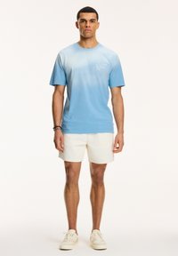 Tricou albastru cu gradient, cu mânecă scurtă, având un guler rotund și un mic print cu logo. Purutat cu şorturi albe și adidași ușori.