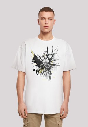 Hvit bomulls t-skjorte med et svart og gult grafisk trykk av en Batman-figur med en stor kappe og stilisert tekst under.