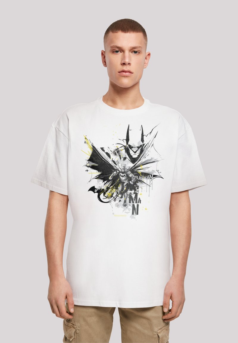 Hvit bomulls t-skjorte med et svart og gult grafisk trykk av en Batman-figur med en stor kappe og stilisert tekst under.