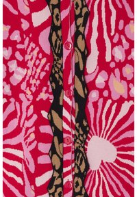 Cárdigan de punto que presenta una mezcla de patrones en rojo, rosa y negro, con botones en contraste y un diseño de borde en forma de ondas.