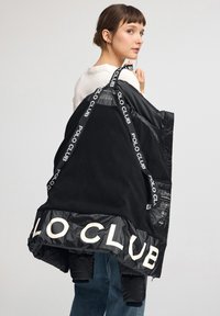 Czarna kurtka z kontrastującą błyszczącą czernią i miękkim materiałem. Posiada logo „POLO CLUB” na dole oraz regulowane paski z nadrukiem marki.