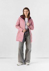 Giacca impermeabile rosa con cappuccio, caratterizzata da un design bicolore, chiusura con zip e tasche laterali, abbinata a jeans larghi grigi e sneakers.
