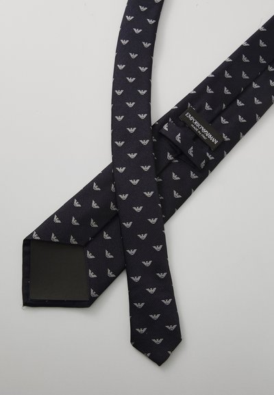 Merijan solmio, jossa on hienovarainen kuviointi pienistä hopeanvärisistä kolmiosaisista motiiveista. Varustettu brändätyllä tarralla ja sileällä pinnalla.