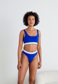 Ensemble de maillots de bain deux pièces bleu comprenant un bralette à encolure dégagée avec une bande d'accent blanche et un bas de bikini taille haute avec des détails assortis.
