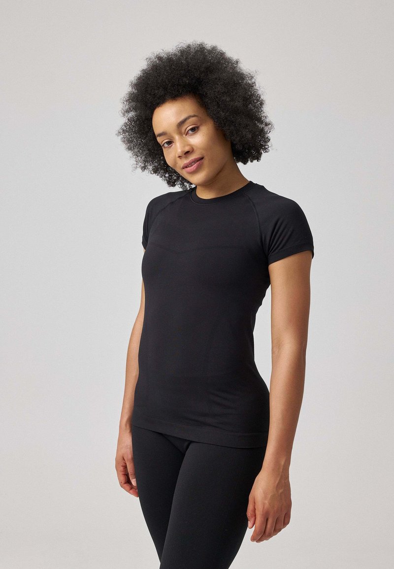 Zwarte, aansluitende t-shirt met korte mouwen, gemaakt van gladde, elastische stof. Heeft een ronde hals en een naadloos schouderontwerp, met een slanke silhouette.